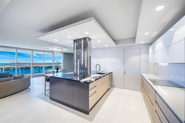 kitchen with light brown cabinets, sink, black electric cooktop, a kitchen breakfast bar, and dark stone countertops