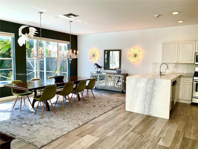 dining room with light wood-type flooring, a healthy amount of sunlight, an inviting chandelier, and sink