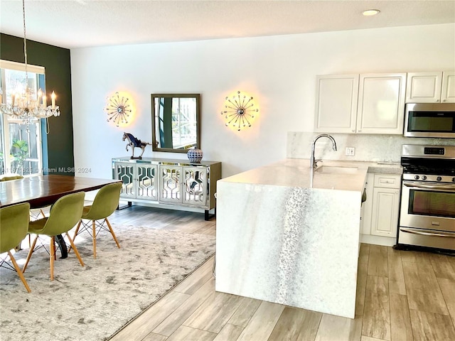 kitchen featuring appliances with stainless steel finishes, white cabinets, kitchen peninsula, light hardwood / wood-style flooring, and decorative light fixtures