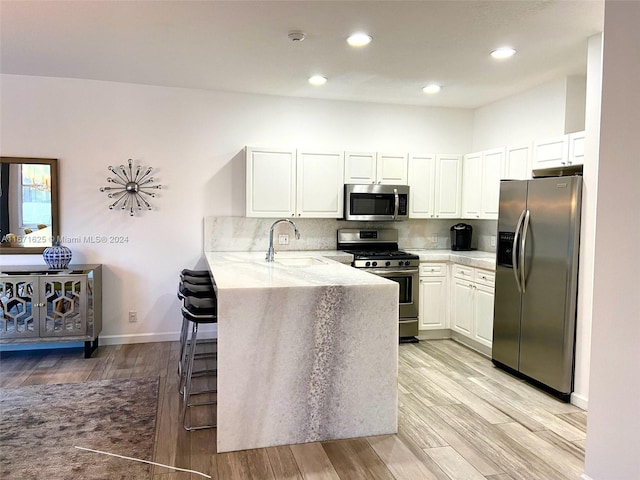 kitchen with light hardwood / wood-style floors, white cabinets, kitchen peninsula, stainless steel appliances, and sink