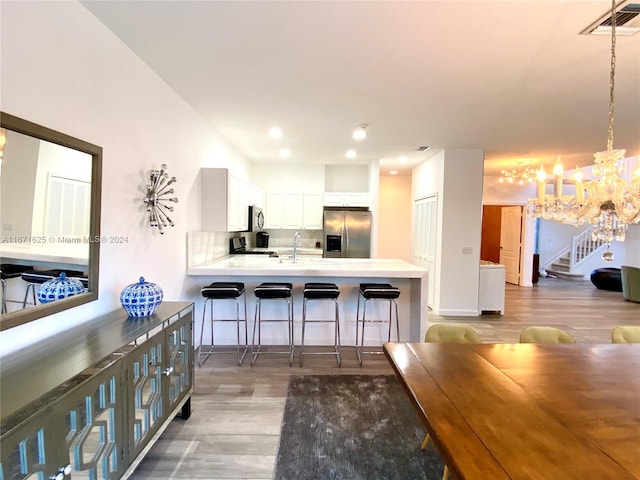 kitchen featuring white cabinetry, kitchen peninsula, a breakfast bar area, stainless steel appliances, and hardwood / wood-style floors