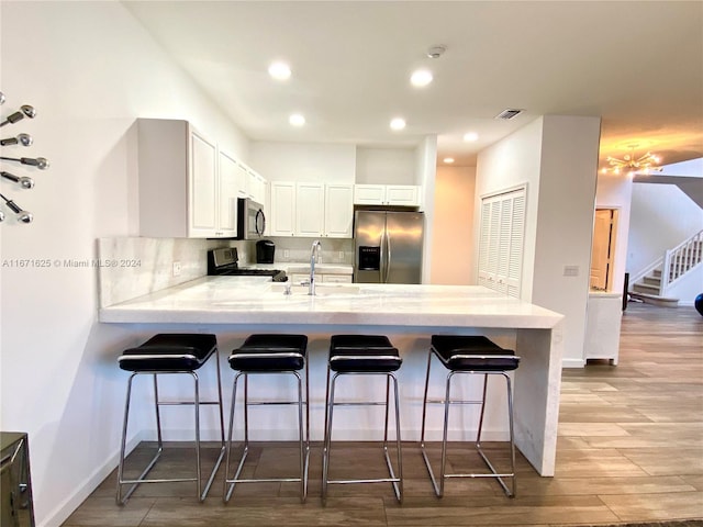 kitchen with a breakfast bar area, white cabinetry, kitchen peninsula, light hardwood / wood-style flooring, and appliances with stainless steel finishes