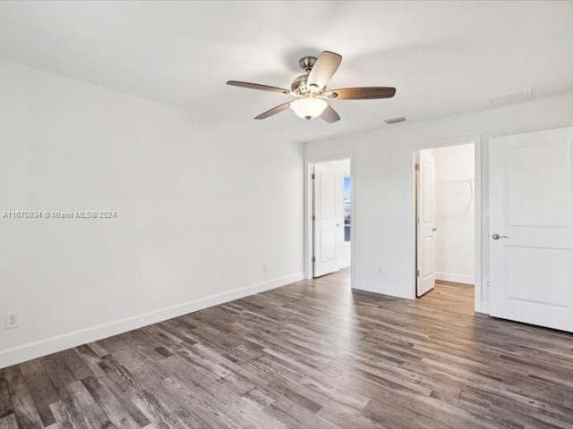 unfurnished bedroom with ceiling fan, a closet, dark wood-type flooring, and a spacious closet