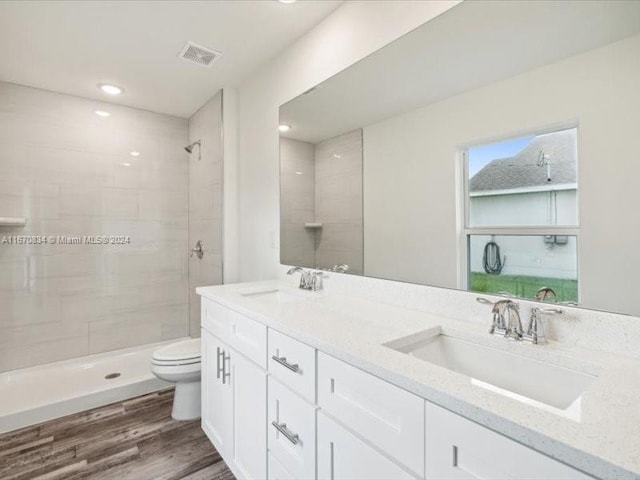 bathroom featuring a tile shower, vanity, hardwood / wood-style floors, and toilet