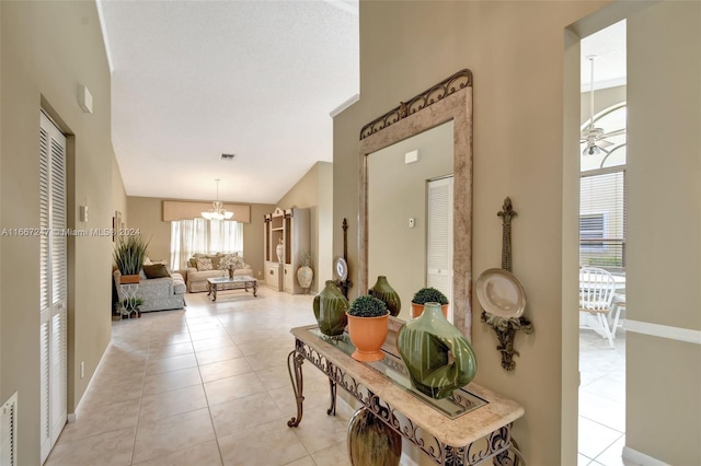 corridor featuring an inviting chandelier, light tile patterned floors, and high vaulted ceiling