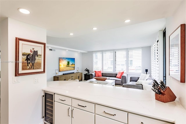 kitchen with wine cooler, white cabinetry, and light stone counters