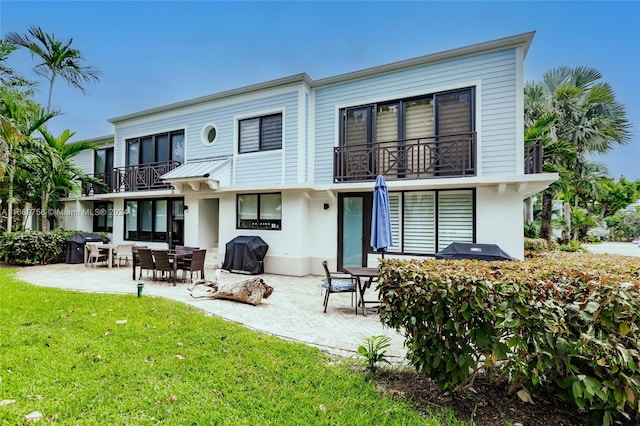 rear view of property featuring a patio area, a yard, and a balcony