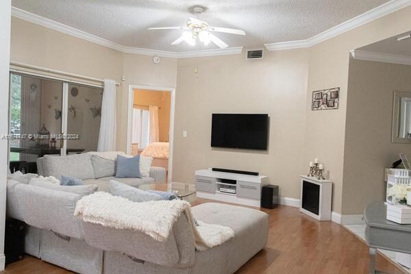 living room with wood-type flooring, a textured ceiling, crown molding, and ceiling fan