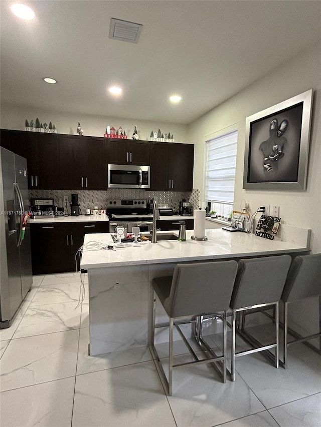 kitchen with stainless steel appliances, kitchen peninsula, a kitchen bar, and tasteful backsplash