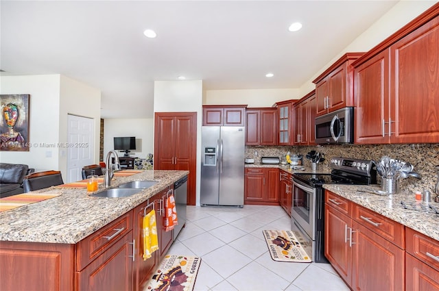 kitchen featuring appliances with stainless steel finishes, a sink, backsplash, light tile patterned floors, and light stone countertops