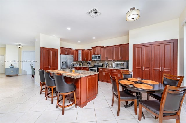 kitchen featuring appliances with stainless steel finishes, tasteful backsplash, glass insert cabinets, an island with sink, and a sink