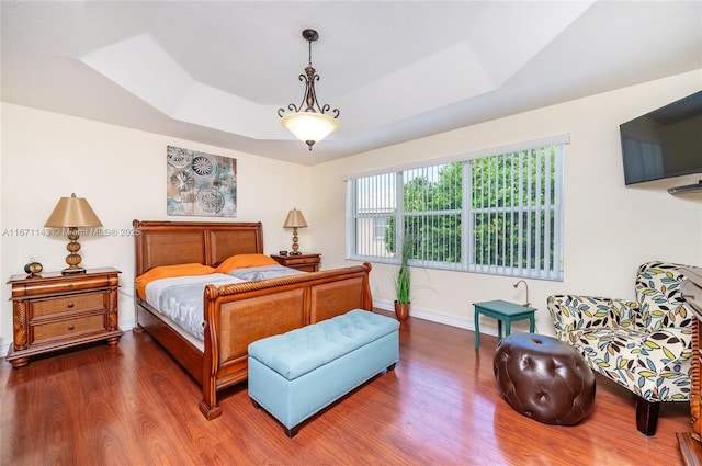 bedroom featuring dark wood finished floors, baseboards, and a raised ceiling