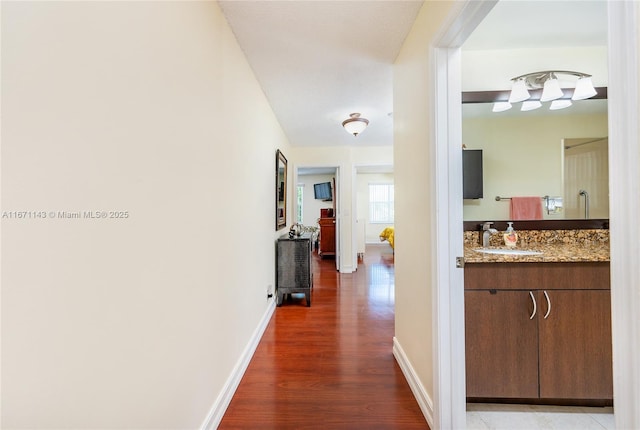 hall with a sink, dark wood-style floors, and baseboards