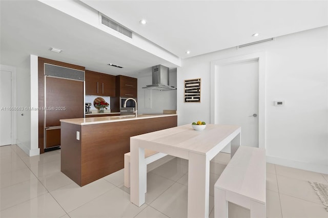 kitchen featuring wall chimney range hood, modern cabinets, paneled built in fridge, and visible vents