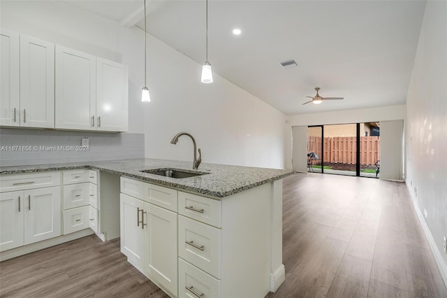 kitchen with tasteful backsplash, light stone countertops, sink, light wood-type flooring, and hanging light fixtures