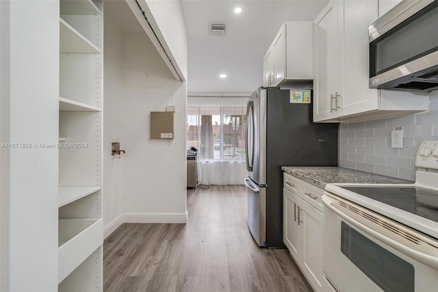 kitchen with stainless steel appliances, light stone countertops, white cabinetry, light hardwood / wood-style floors, and tasteful backsplash