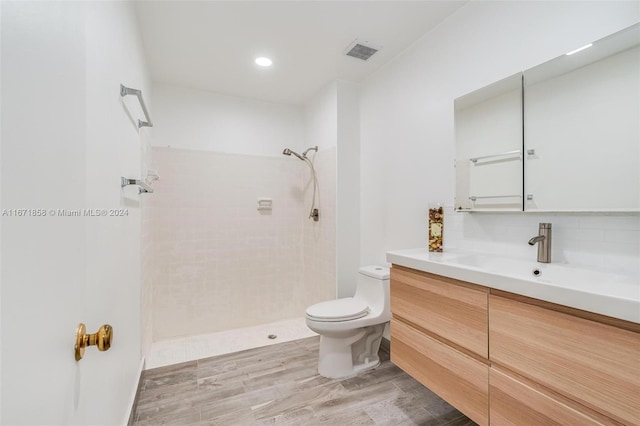 bathroom with backsplash, a tile shower, hardwood / wood-style flooring, toilet, and vanity