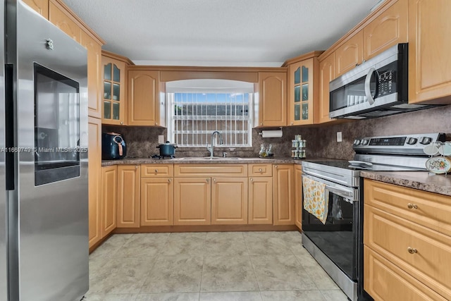 kitchen featuring sink, stainless steel appliances, dark stone counters, decorative backsplash, and light tile patterned flooring