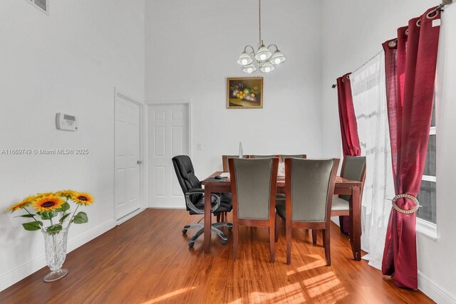 dining room featuring hardwood / wood-style floors, a towering ceiling, and an inviting chandelier