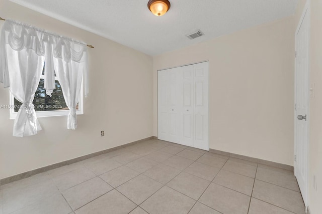 unfurnished bedroom featuring a closet, light tile patterned floors, and a textured ceiling