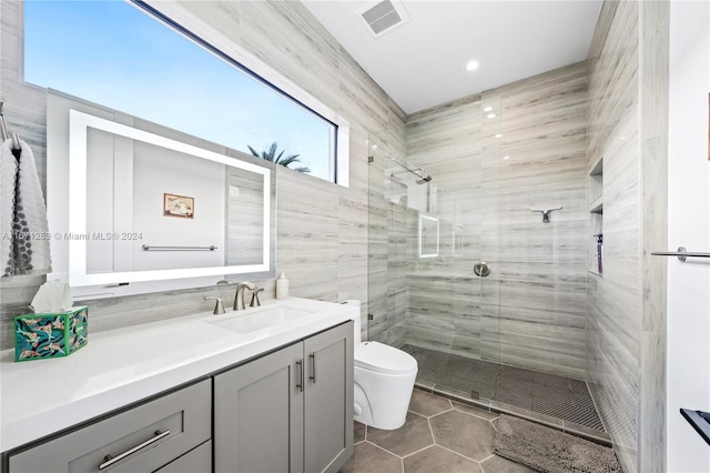 bathroom with tile walls, toilet, vanity, an enclosed shower, and tile patterned flooring