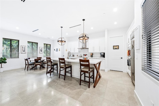 kitchen with white cabinets, hanging light fixtures, a center island with sink, a breakfast bar area, and backsplash