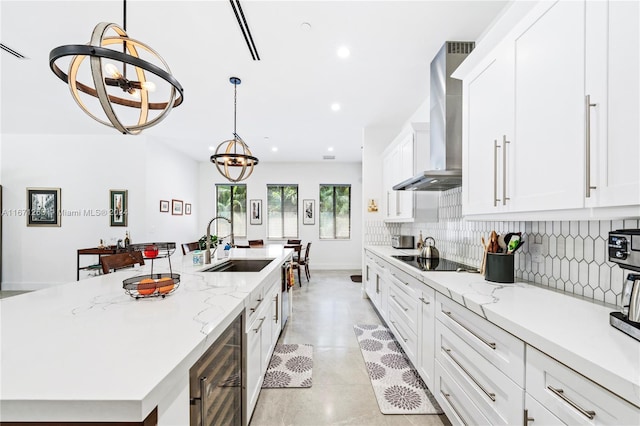 kitchen featuring wall chimney range hood, white cabinetry, a chandelier, and beverage cooler