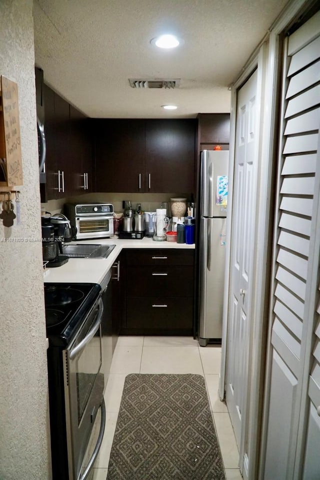 kitchen with stainless steel appliances, a textured ceiling, light tile patterned flooring, and dark brown cabinetry