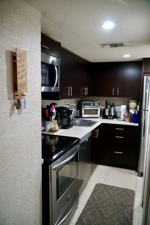 kitchen with light tile patterned flooring, sink, dark brown cabinets, a textured ceiling, and stainless steel appliances