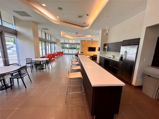 kitchen with hanging light fixtures, a tray ceiling, stainless steel fridge, a center island, and a kitchen bar