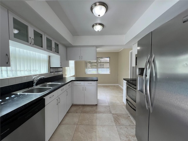 kitchen featuring appliances with stainless steel finishes, white cabinetry, kitchen peninsula, light tile patterned floors, and sink