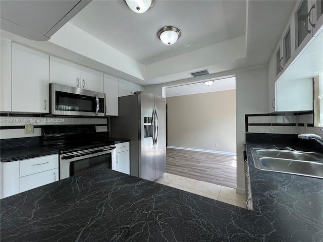 kitchen with appliances with stainless steel finishes, decorative backsplash, white cabinets, light wood-type flooring, and sink