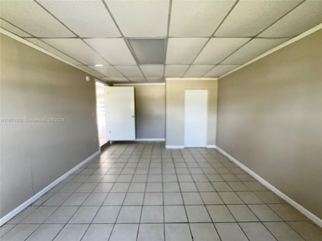 tiled empty room with a drop ceiling and crown molding