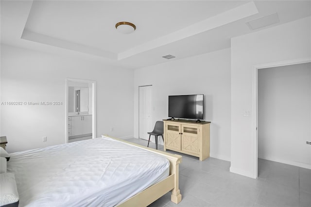 bedroom with a raised ceiling, ensuite bath, tile patterned floors, and a closet