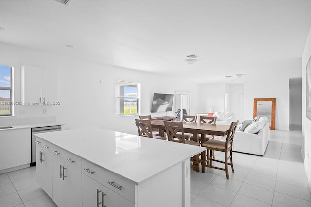 kitchen featuring a kitchen island, stainless steel dishwasher, white cabinetry, and light tile patterned flooring