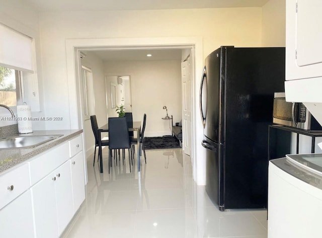 kitchen featuring white cabinets, black fridge, light tile patterned floors, sink, and stacked washer / drying machine