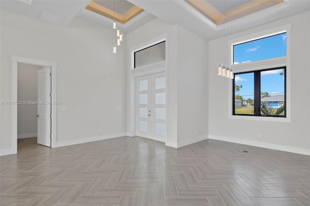 empty room with light parquet floors, a tray ceiling, a towering ceiling, and french doors