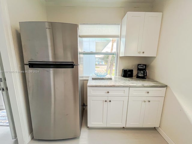 kitchen featuring white cabinetry, stainless steel fridge, and light stone counters