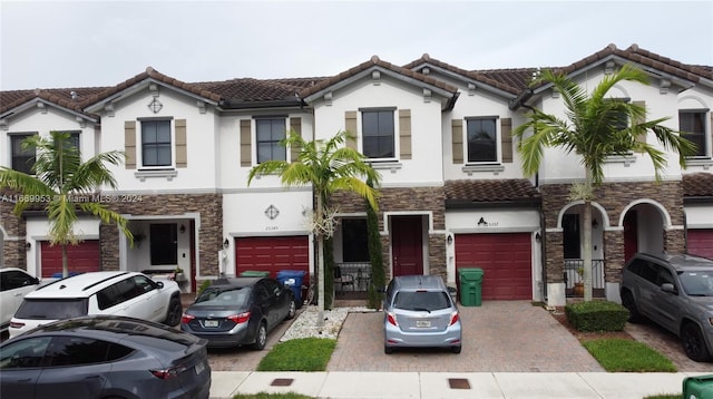 view of property featuring stucco siding, stone siding, a tile roof, an attached garage, and driveway
