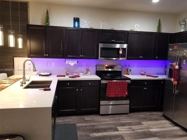 kitchen featuring dark wood finished floors, a peninsula, light countertops, a sink, and stainless steel appliances