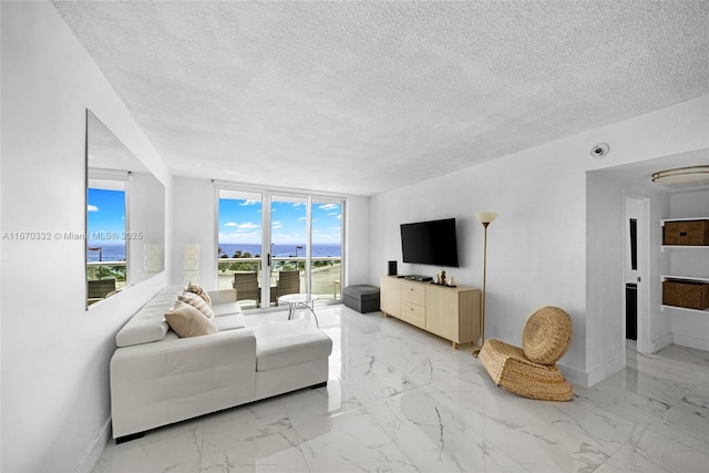 living area featuring a textured ceiling, marble finish floor, a wall of windows, and baseboards