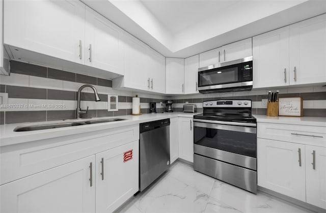 kitchen featuring stainless steel appliances, marble finish floor, a sink, and backsplash