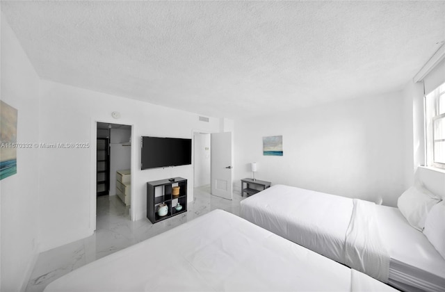 bedroom featuring marble finish floor, visible vents, a textured ceiling, and a spacious closet