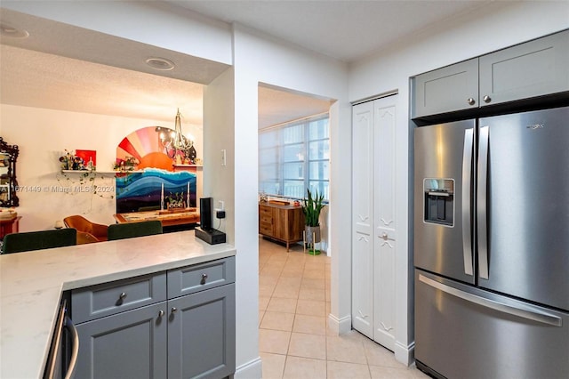 kitchen with gray cabinets, stainless steel fridge, light tile patterned floors, a textured ceiling, and a chandelier