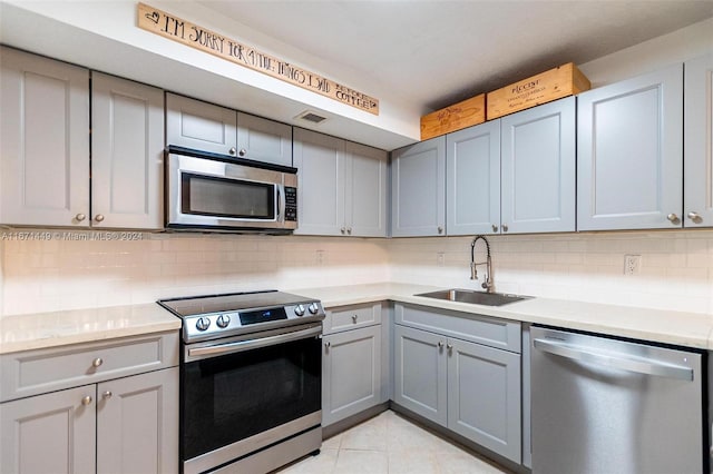 kitchen featuring gray cabinetry, backsplash, sink, appliances with stainless steel finishes, and light tile patterned flooring