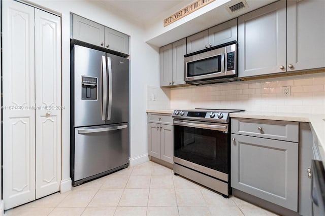 kitchen with backsplash, gray cabinets, light tile patterned floors, and stainless steel appliances