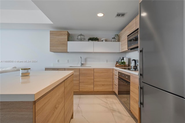 kitchen with black appliances, light brown cabinetry, a kitchen island, and sink