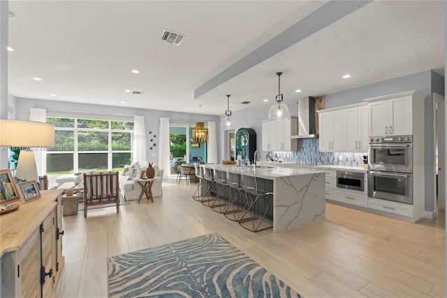 kitchen with white cabinetry, a wealth of natural light, wall chimney exhaust hood, and pendant lighting