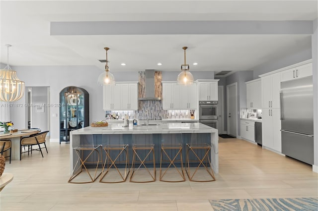 kitchen featuring white cabinets, appliances with stainless steel finishes, decorative light fixtures, and wall chimney range hood