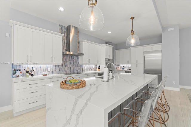 kitchen with appliances with stainless steel finishes, white cabinetry, a large island with sink, and wall chimney exhaust hood